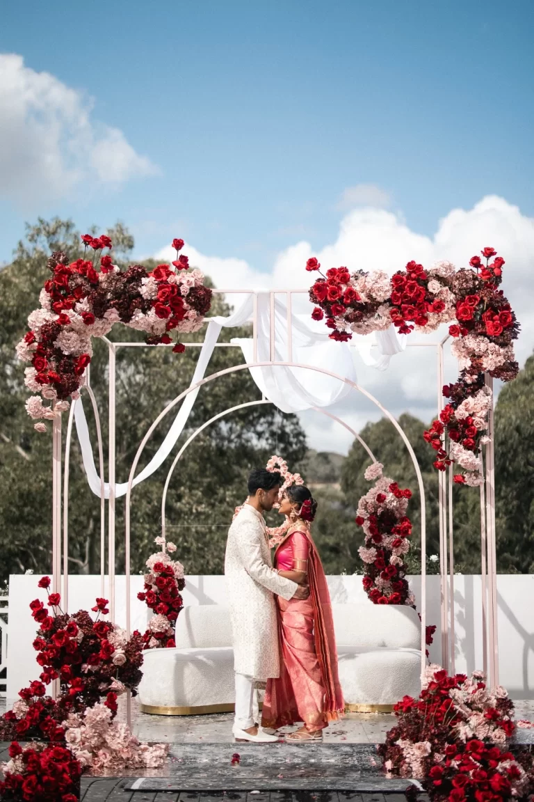A Hindu couple under floral arch following outdoor wedding ceremony